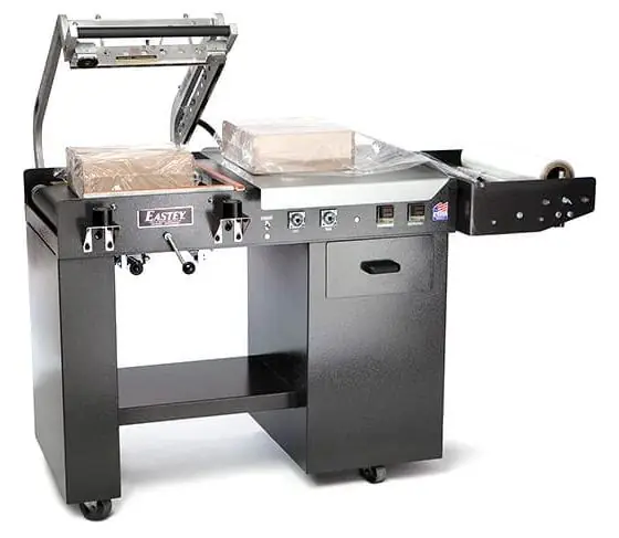 A floor-standing L-sealer with the seal head raised, film cradle, and takeaway conveyor.