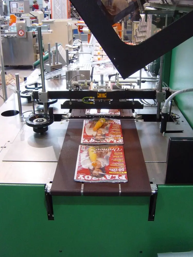 A horizontal wrapping machine with a conveyor carrying magazines wrapped in clear film.