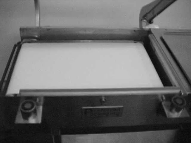 A closed L-bar seal head resting on a white product tray, with a round magnet at each front corner.