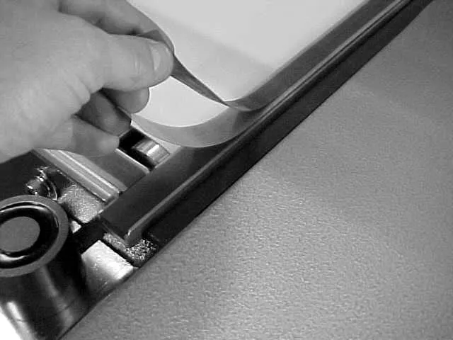 A hand pressing a strip of PTFE tape onto the seal pad along the lower jaw of an L-bar sealer.