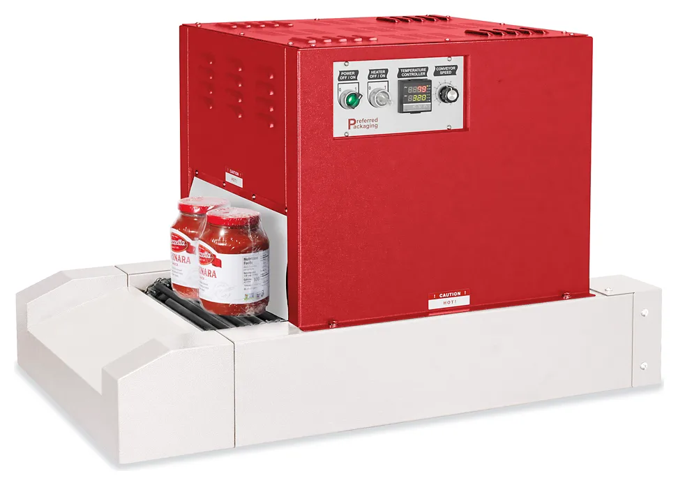 A red tabletop shrink tunnel on a white conveyor base, with a temperature controller and conveyor speed knob on the front and two wrapped jars entering the chamber.